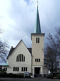 Hohes Kirchengebäude mit markantem Turm, heller Fassade und Bäumen.
