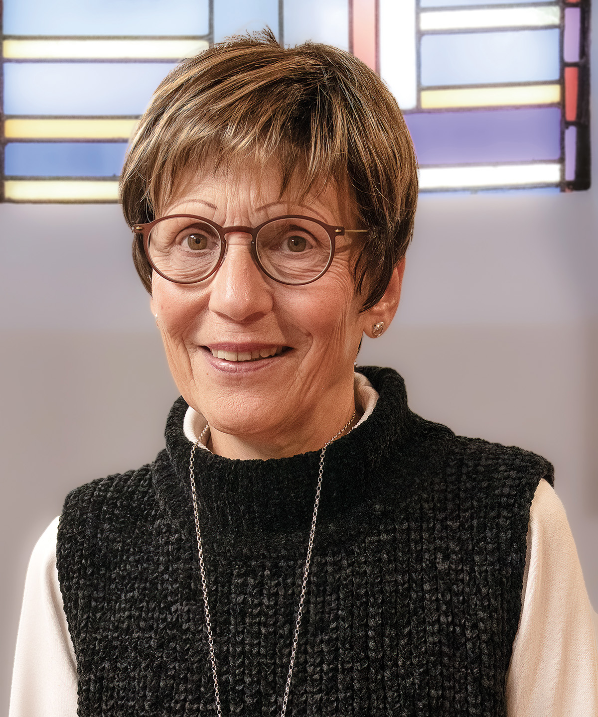 Lächelnde Frau mit kurzen Haaren, Brille und dunklem Pullover.