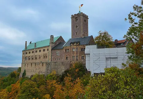Wartburg auf einem Hügel, umgeben von Herbstlaub unter bewölktem Himmel.