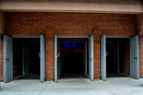 Drei offene graue Türen in einem braunen Backsteingebäude.