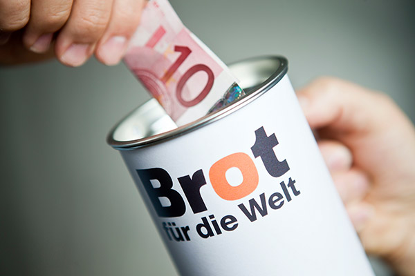 Hand steckt Zehn-Euro-Schein in "Brot für die Welt" Spendenbüchse.