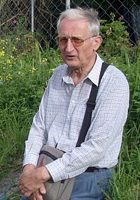 Älterer Mann mit Brille und Umhängetasche im Freien.