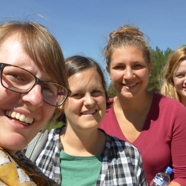 Vier lächelnde Frauen posieren für ein Outdoor-Selfie.