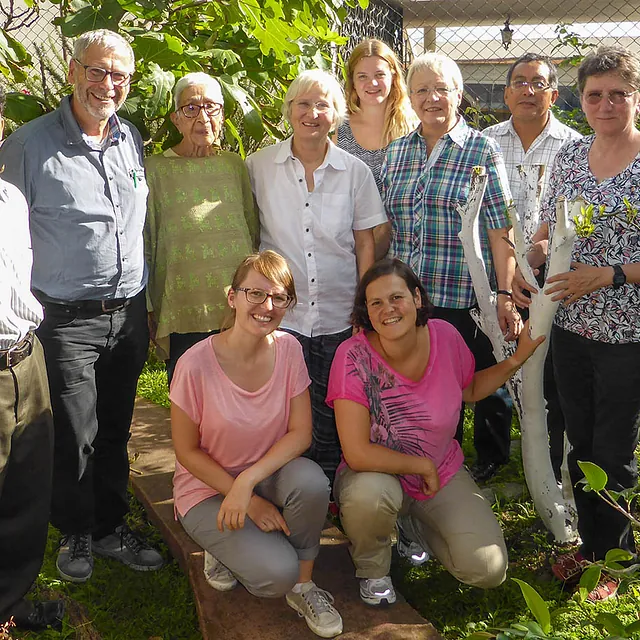 Vielfältige Gruppe von Menschen lächelt zusammen in sonnigem Garten.