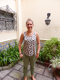 Junge Frau mit Dutt steht in Hof mit gemusterten Fliesen.