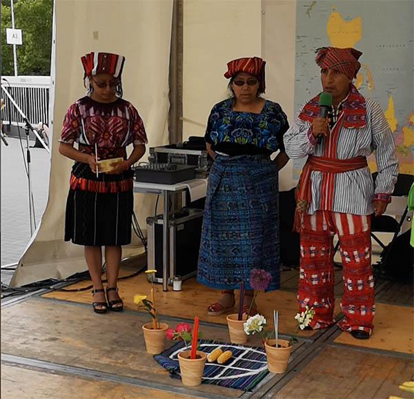 Indigene Frauen in Tracht treten auf, Mann spricht ins Mikrofon.