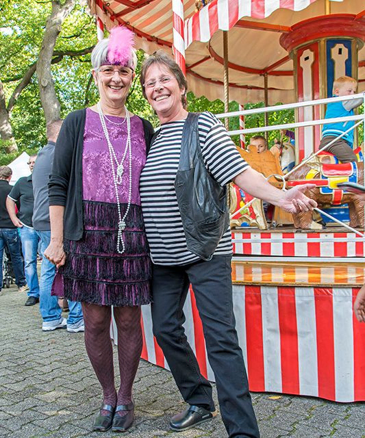 Zwei fröhliche Frauen posieren draußen an einem klassischen Karussell.