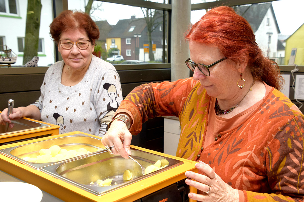  Zwei Frauen bedienen sich an einem Buffet, eine mit roten Haaren.