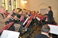 Dirigent leitet ein Orchester, das Blasinstrumente im Innenbereich spielt.