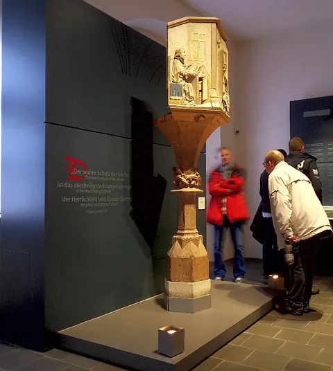 Ornate historische Holzkanzel ausgestellt in einem Museum mit Besuchern.