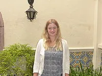 Blondhaarige Frau lächelt in Hof mit gemusterten Fliesen.