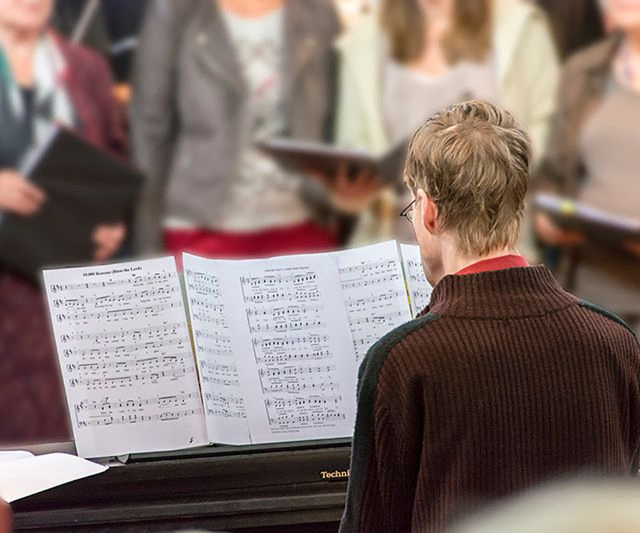 Person von hinten spielt Klavier mit Noten, Chor unscharf."
