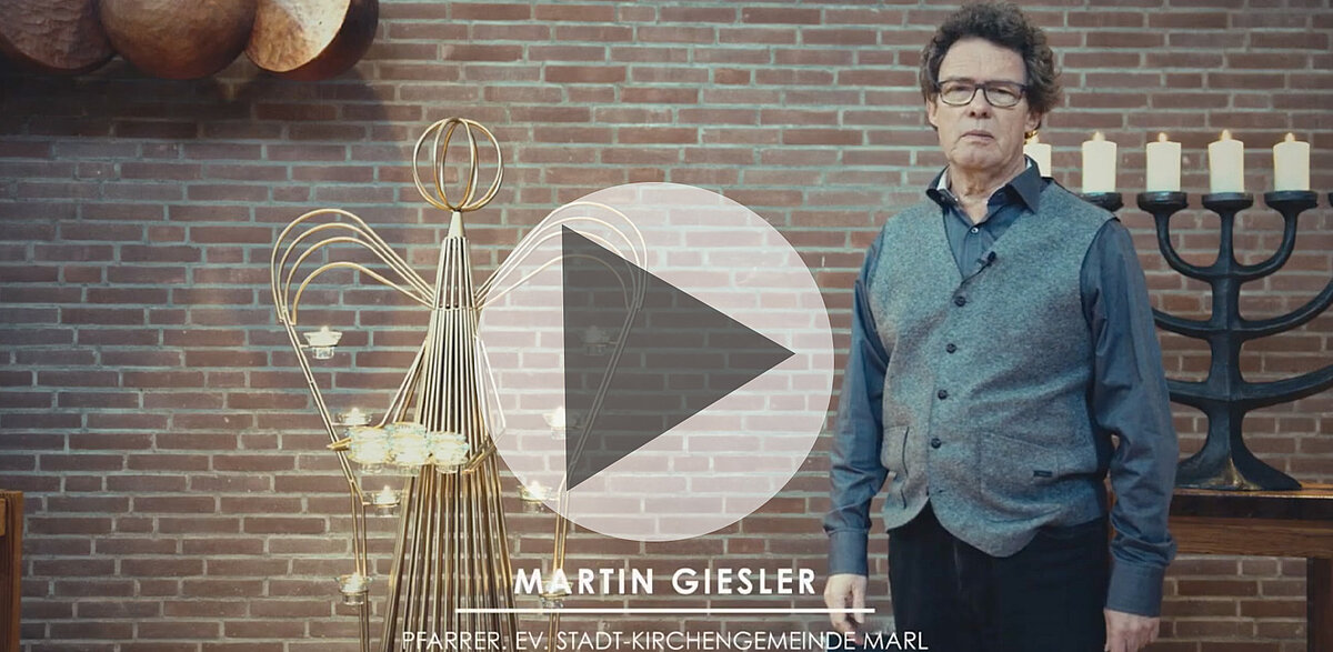 Martin Giesler, Pfarrer, steht in Kirche mit Engel und Kerzen.