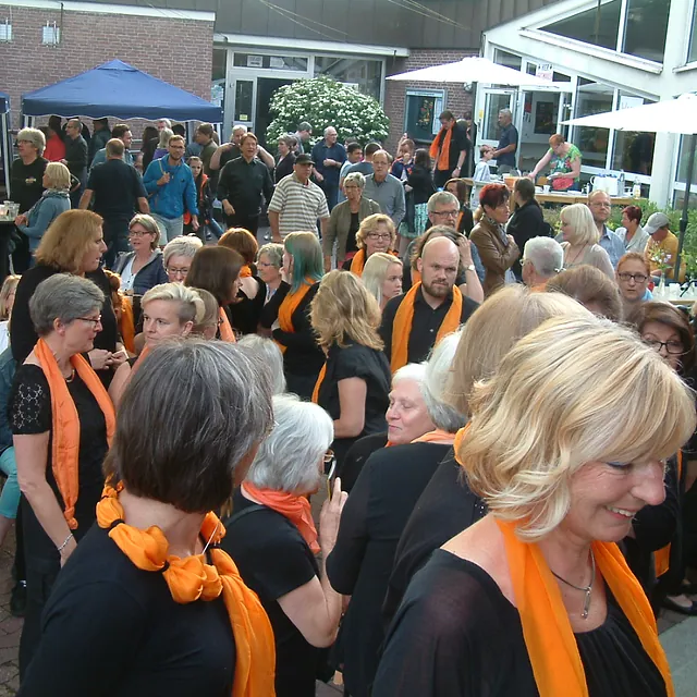 Eine Gruppe Menschen, viele mit orangefarbenen Schals, bei einem Treffen im Freien.