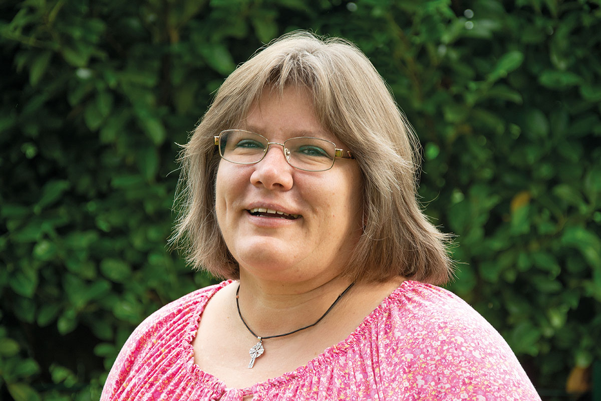 Eine lächelnde Frau mit Brille und gemustertem rosa Hemd.