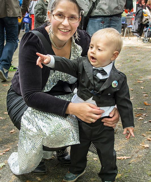 Lächelnde Frau mit Kind in festlicher Kleidung, zeigend.