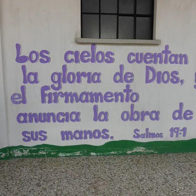 Lila spanische Schrift aus Salmos 19:1 auf weißer Wand gemalt.