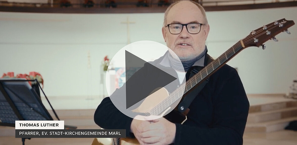Pfarrer Thomas Luther mit Gitarre, spricht Zuschauer in Kirche an.