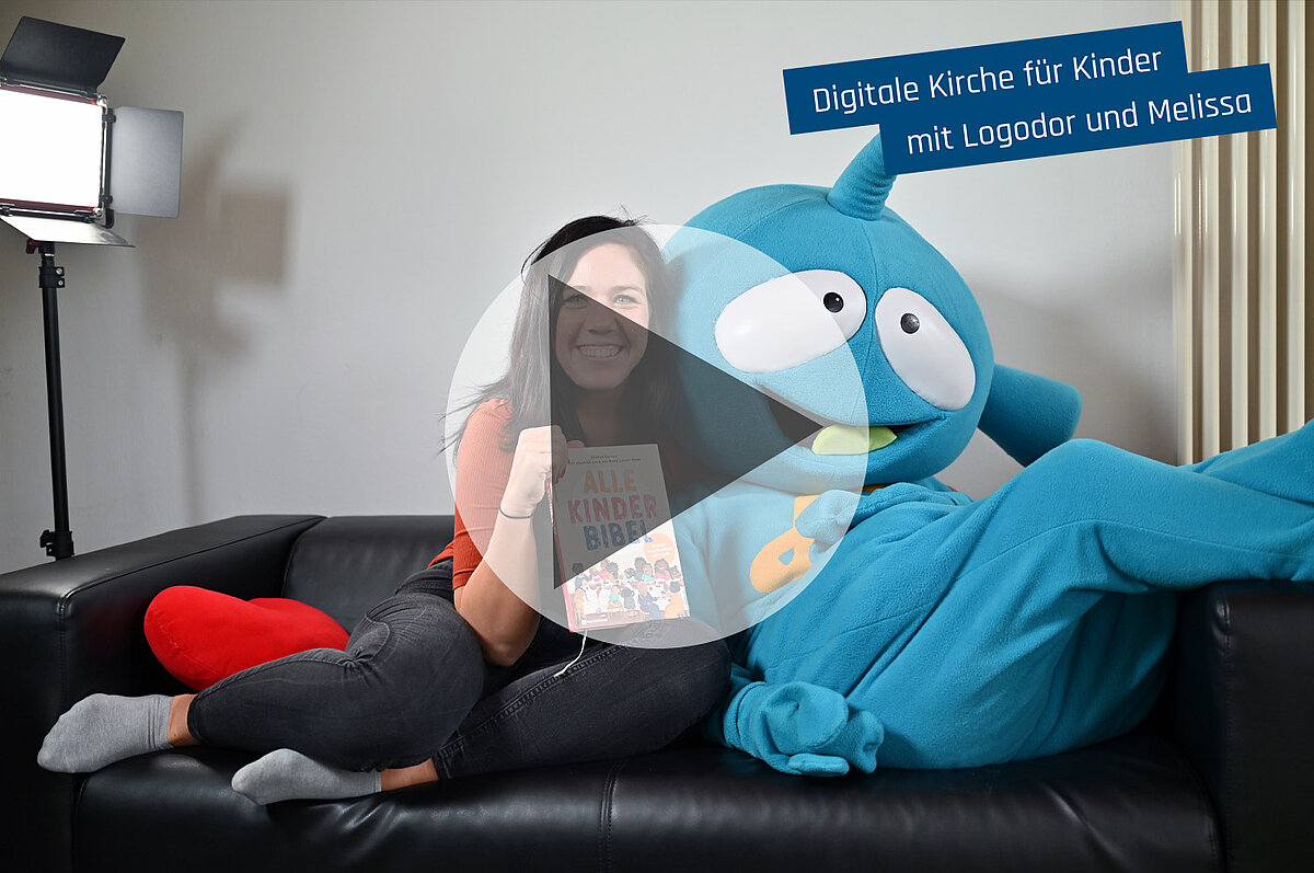 Lächelnde Frau und blaues Maskottchen mit "Kinder Bibel" auf Sofa.