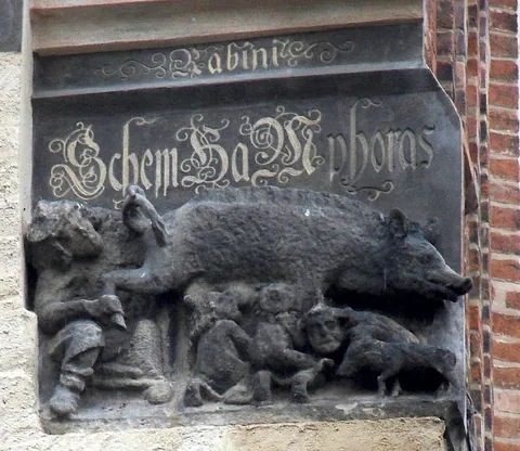 Kontroverses historisches Relief "Judensau" an Gebäude, Figuren und Schwein darstellend.