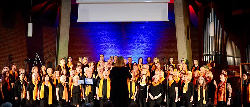 Choraufführung in Kirche mit Dirigentin, blaue und rote Beleuchtung.
