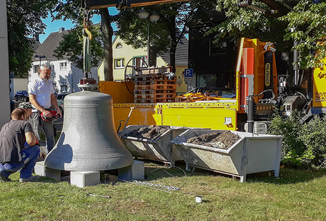 Große Glocke ruht auf Blöcken, Arbeiter inspizieren sie genau.