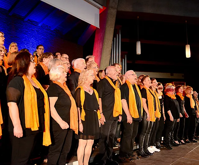Lebhafter Gospelchor tritt auf der Bühne auf, vielfältige Sänger in orangefarbenen Schals.