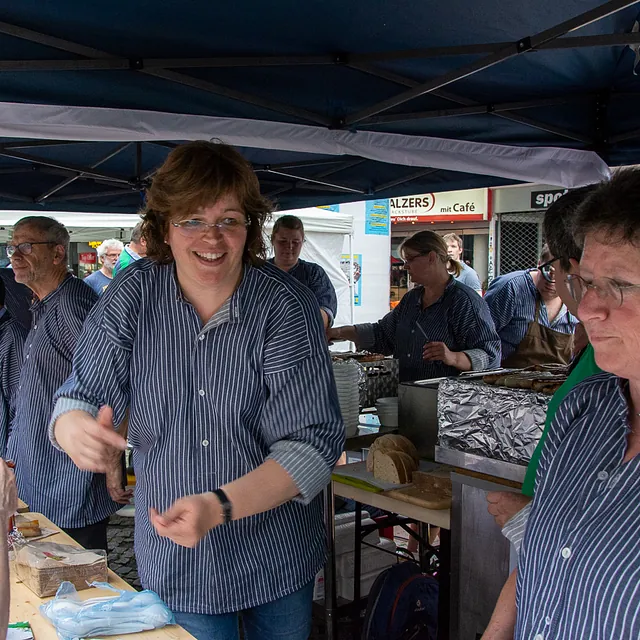 Lächelnde Frau arbeitet an einem geschäftigen Marktstand.