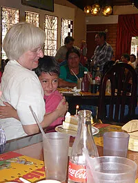 Frau umarmt ein Kind an einem Tisch mit Kuchen und Getränken.