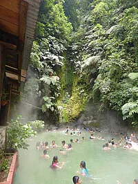 Menschen baden in einer natürlichen heißen Quelle inmitten üppigen Grüns.