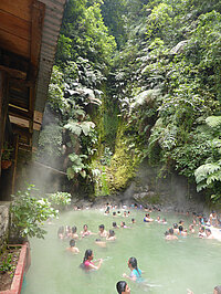 Menschen baden in einer natürlichen heißen Quelle inmitten üppigen Grüns.