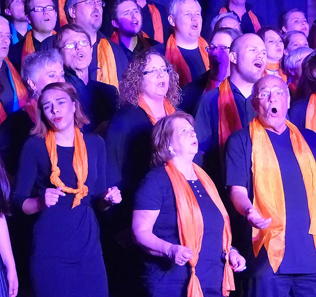Vielfältige Gruppe von Chormitgliedern singt leidenschaftlich in orangefarbenen Schals.