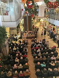 Große Versammlung in einem geschmückten Einkaufszentrum, mit Chorauftritt.