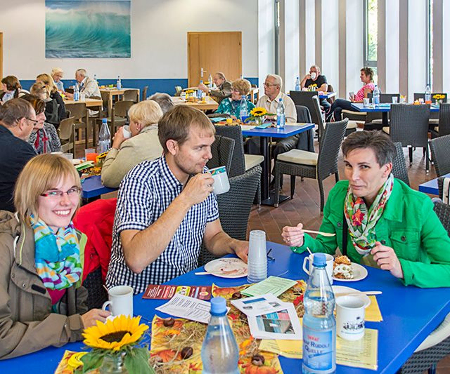 Diverse Gruppe von Menschen genießt Essen und Getränke an Tischen.