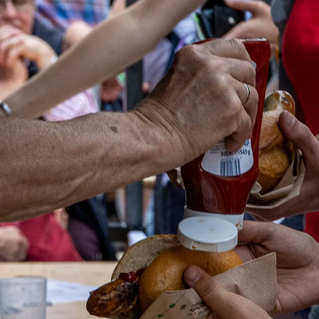 Hände geben Ketchup auf eine Wurst im Brötchen.