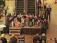 Kinderchor tritt auf Bühne auf, Erwachsene schauen zu.