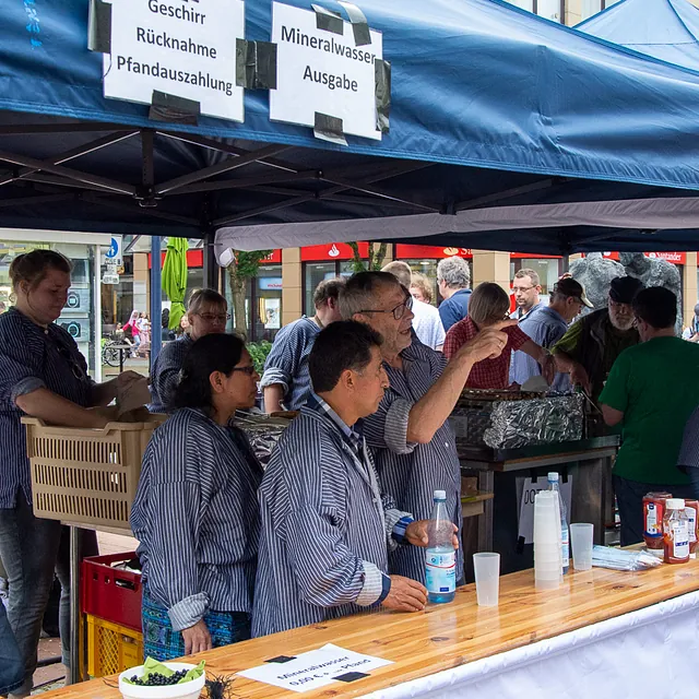 Belebter Essensstand auf einem Markt, Leute bedienen und kaufen.
