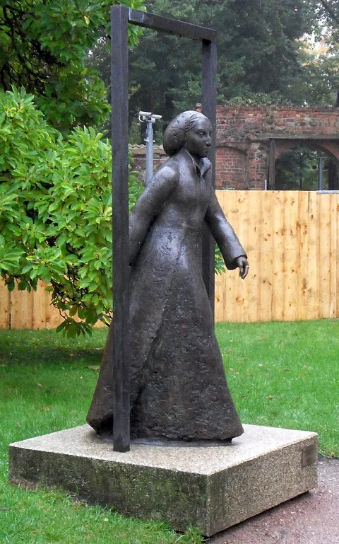 Bronzestatue einer Frau in langem Kleid im Freien, gerahmt.
