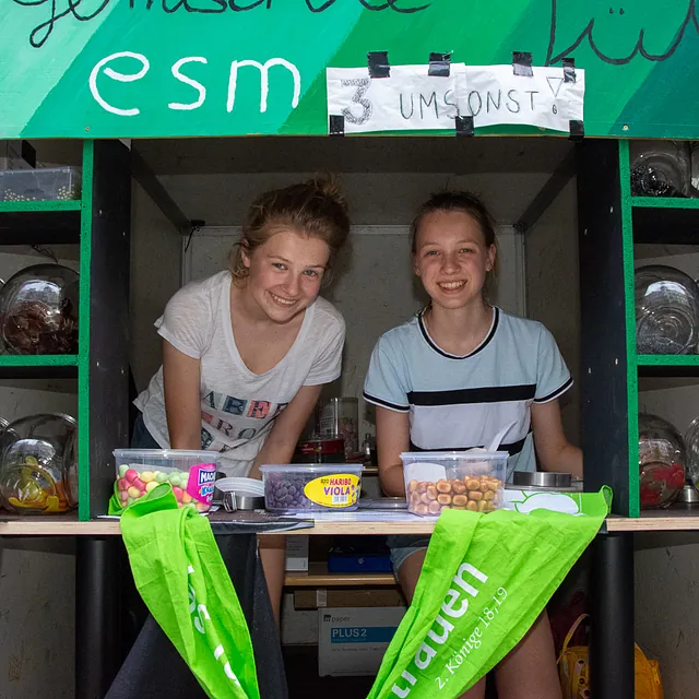 Zwei lächelnde junge Frauen an einem Marktstand.
