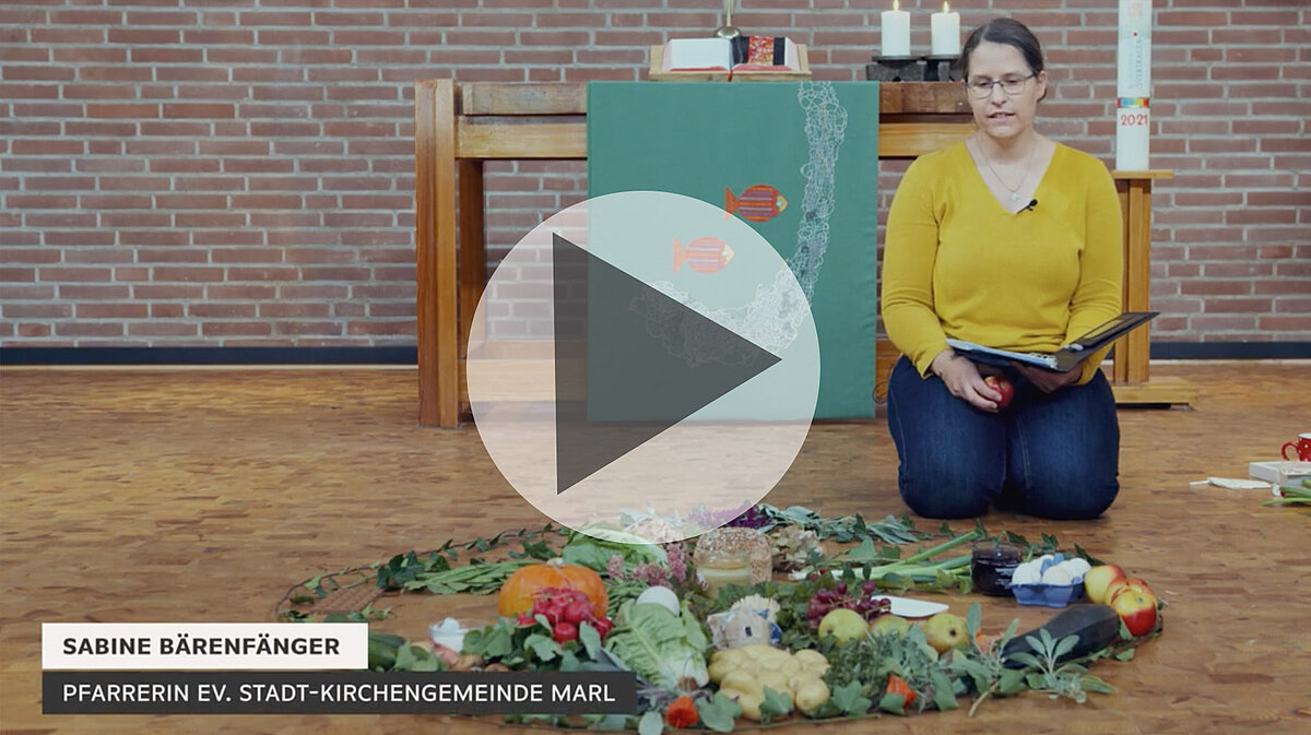 Pfarrerin Sabine Bärenfänger sitzt mit Erntedankdekoration in der Kirche.