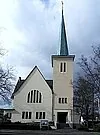 Weiße Kirche mit hohem grünem Turm unter bewölktem Himmel.