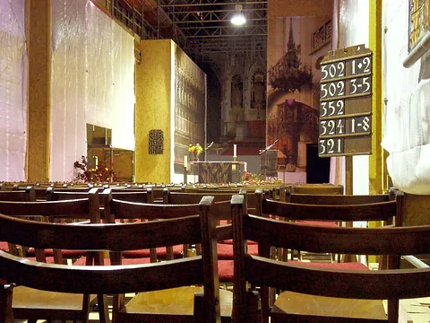 Kircheninneres mit Holzreihen, Altar und Gesangbuchtafel.