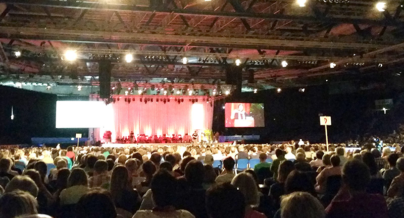 Großes Publikum in Arena betrachtet Bühnenauftritt und Bildschirm.