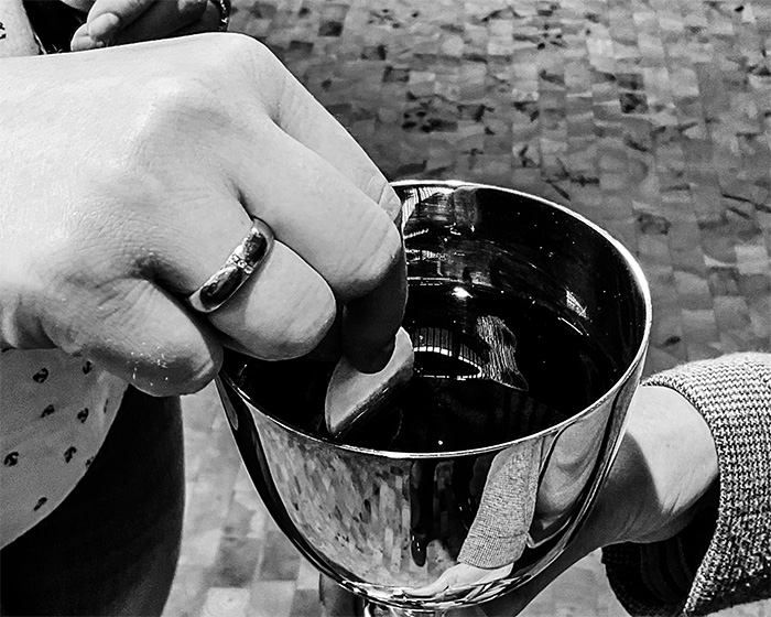 Eine Hand taucht eine Oblate in den Abendmahlskelch